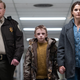 A police officer, a small boy, and teacher (all looking worried) walk together down a hallway in a scene from horror film Antlers.